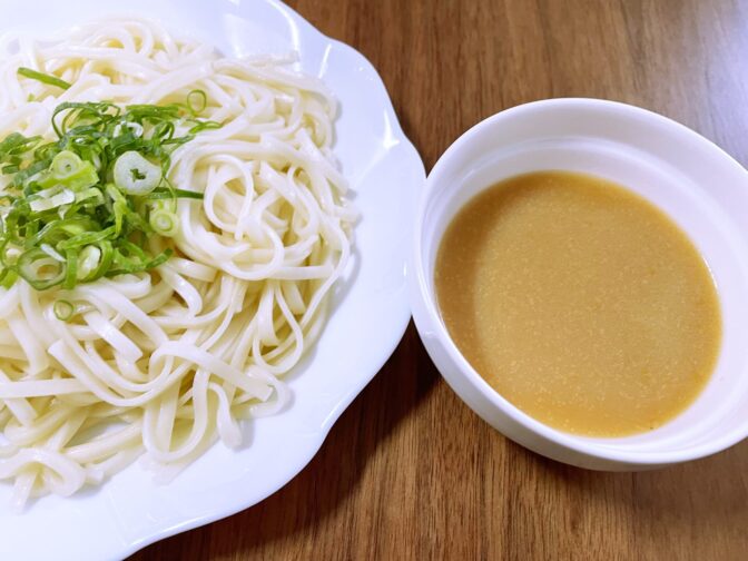 熱々のうどんに九条ネギを盛り、冷たいゴマ味噌麺つゆはお好みで水で薄めます。